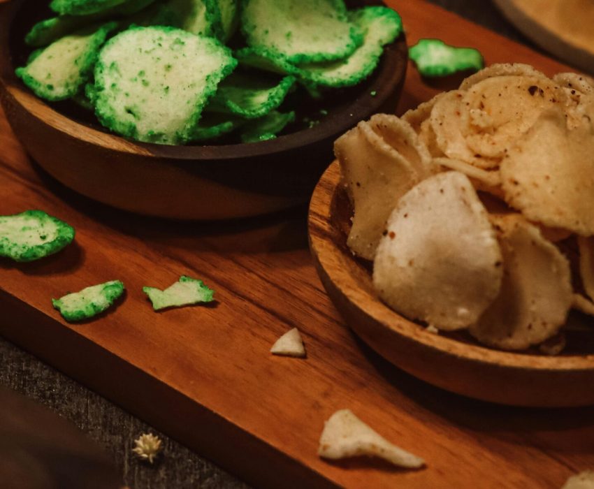 Assorted flavored chips in bowls on a wooden tray, showcasing a delicious snack variety.